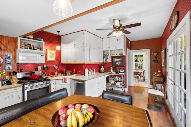 kitchen with appliances with stainless steel finishes, ceiling fan, hanging light fixtures, hardwood / wood-style floors, and white cabinets