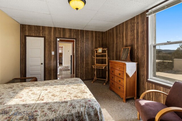 bedroom featuring a drop ceiling, dark colored carpet, and wooden walls