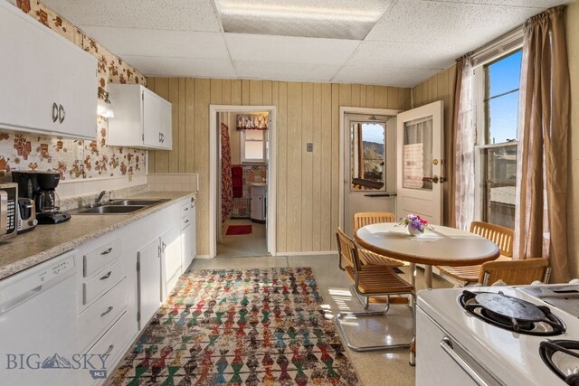 kitchen with a drop ceiling, wooden walls, sink, white cabinetry, and white appliances