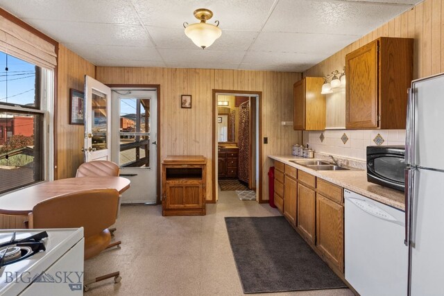 kitchen featuring dishwasher, wooden walls, sink, and stainless steel refrigerator