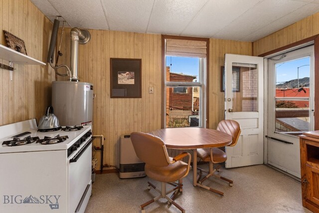 kitchen with water heater, wooden walls, a healthy amount of sunlight, and white gas range oven