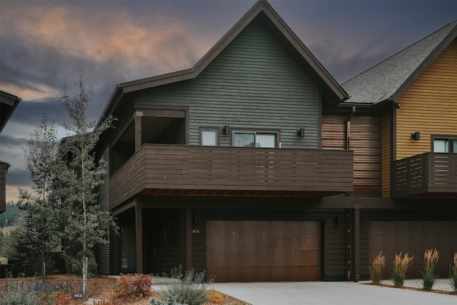 back house at dusk with a garage and a balcony