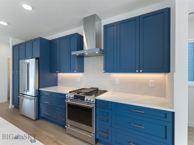 kitchen featuring wall chimney range hood, decorative backsplash, blue cabinetry, and high end appliances