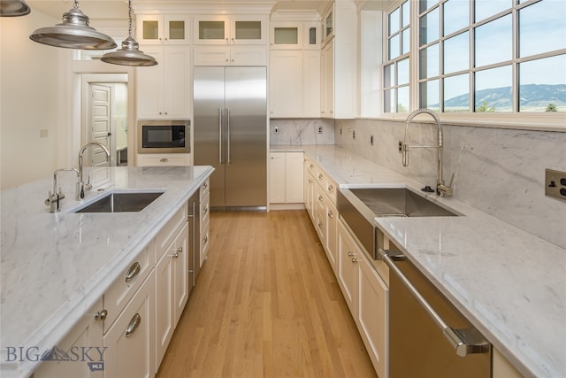 kitchen with light stone counters, a mountain view, decorative light fixtures, built in appliances, and sink