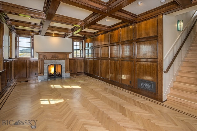 unfurnished living room with light parquet floors, a premium fireplace, wood walls, coffered ceiling, and beam ceiling