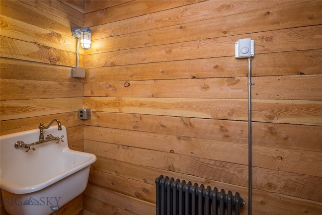 bathroom with a washtub, radiator heating unit, wood walls, and sink