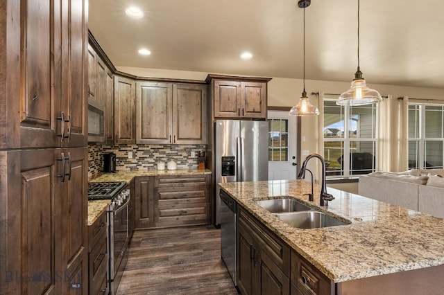 kitchen with appliances with stainless steel finishes, sink, pendant lighting, dark hardwood / wood-style floors, and an island with sink