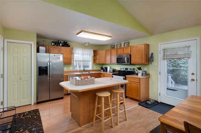 kitchen featuring stainless steel appliances, a kitchen island, sink, lofted ceiling, and light hardwood / wood-style flooring