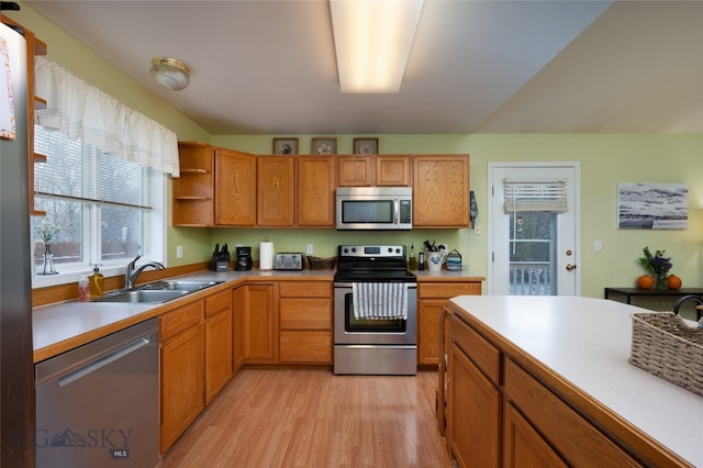 kitchen with appliances with stainless steel finishes, sink, and light hardwood / wood-style flooring