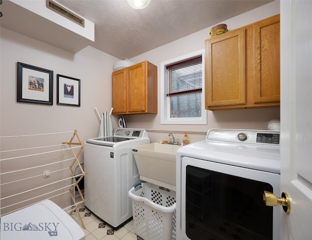 washroom with washing machine and clothes dryer, cabinets, and a textured ceiling