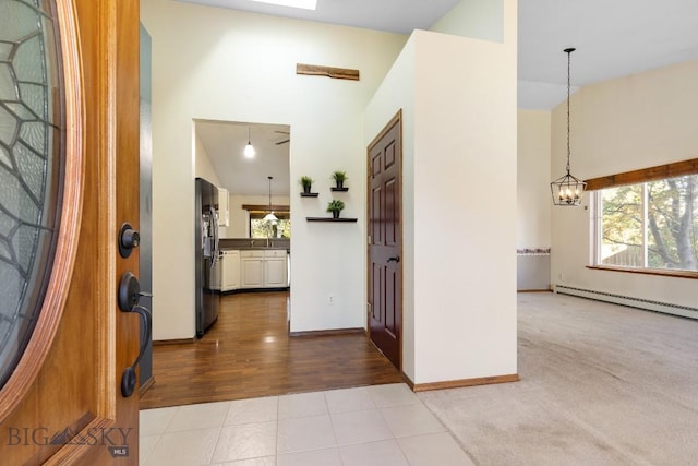 corridor featuring a notable chandelier, a baseboard heating unit, light tile patterned floors, and high vaulted ceiling