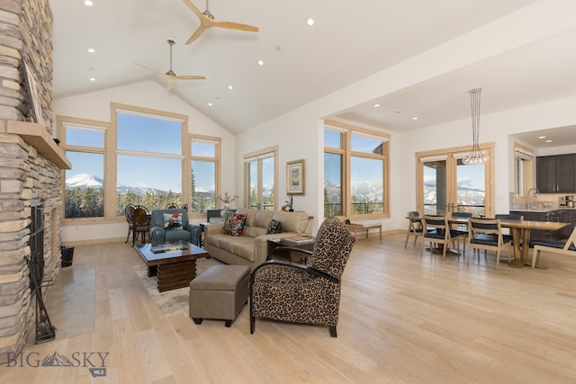 living room with light hardwood / wood-style floors, a mountain view, a stone fireplace, and high vaulted ceiling