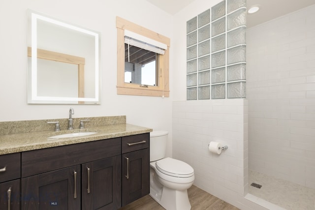 bathroom featuring toilet, vanity, wood-type flooring, and tiled shower