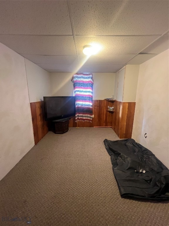 interior space with a paneled ceiling, carpet flooring, and wooden walls