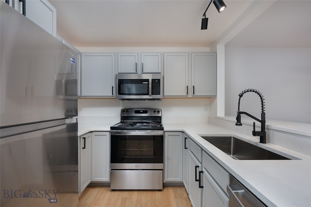 kitchen with sink, rail lighting, stainless steel appliances, and light hardwood / wood-style floors