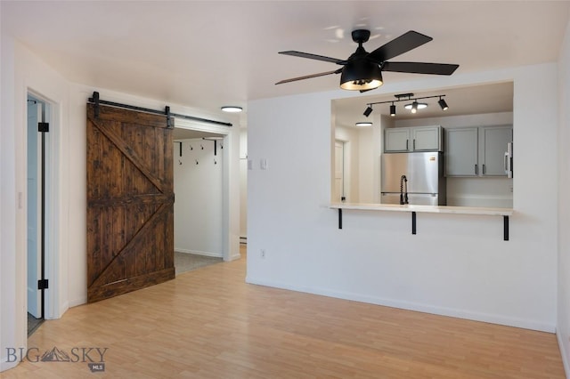 interior space with ceiling fan, a barn door, and light hardwood / wood-style flooring