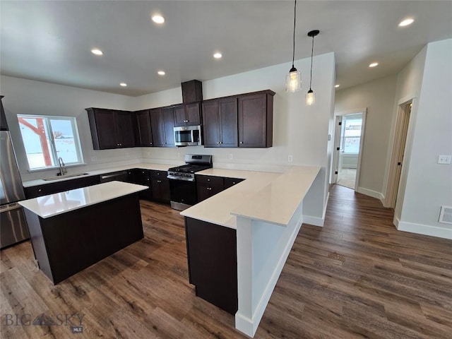 kitchen featuring decorative light fixtures, light countertops, appliances with stainless steel finishes, a sink, and a peninsula