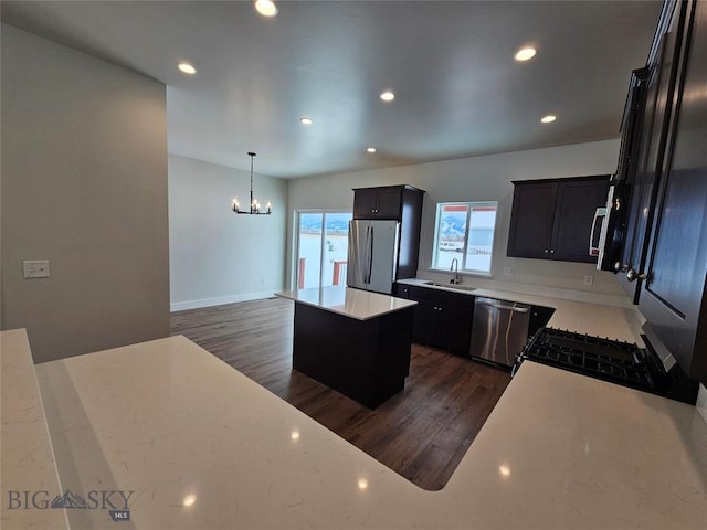 kitchen with a center island, dark wood-style flooring, hanging light fixtures, appliances with stainless steel finishes, and a sink