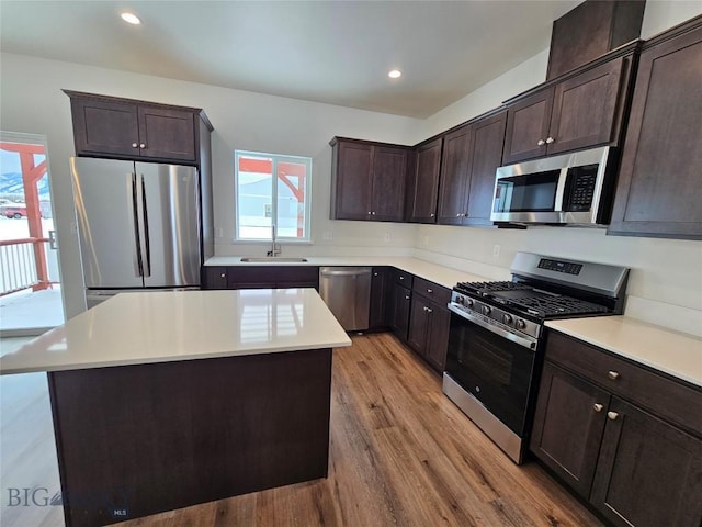 kitchen featuring stainless steel appliances, a sink, dark brown cabinets, light countertops, and a center island