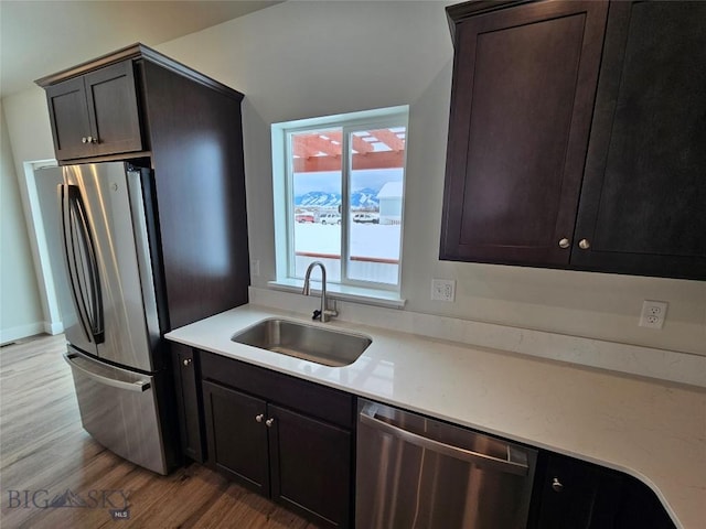 kitchen with dark brown cabinetry, stainless steel appliances, a sink, and light countertops