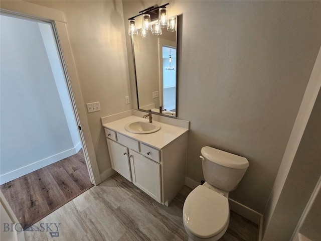 bathroom featuring toilet, baseboards, wood finished floors, and vanity