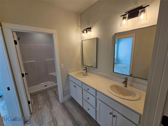 bathroom featuring double vanity, a shower stall, a sink, and wood finished floors