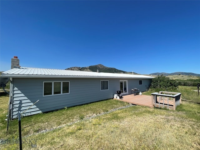 back of house with a deck with mountain view and a lawn