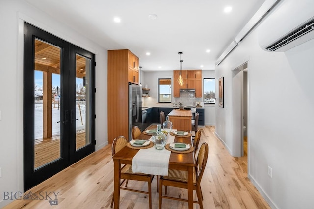 dining room with a wall mounted air conditioner, light hardwood / wood-style flooring, and french doors