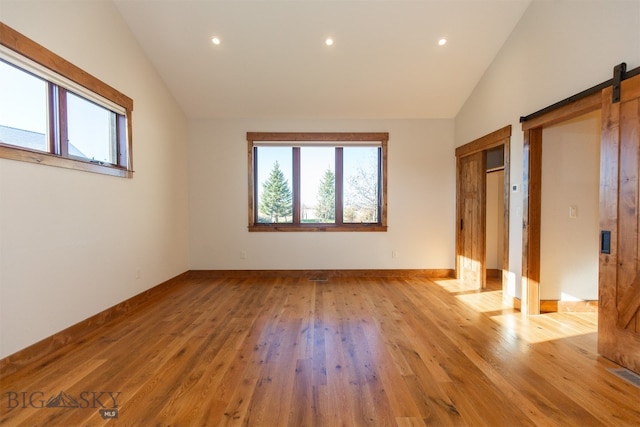 spare room featuring a barn door, light hardwood / wood-style flooring, and high vaulted ceiling