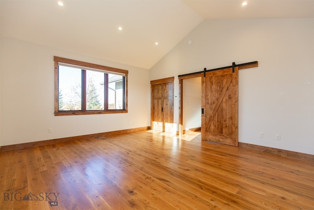 unfurnished bedroom featuring light hardwood / wood-style floors, a barn door, and high vaulted ceiling