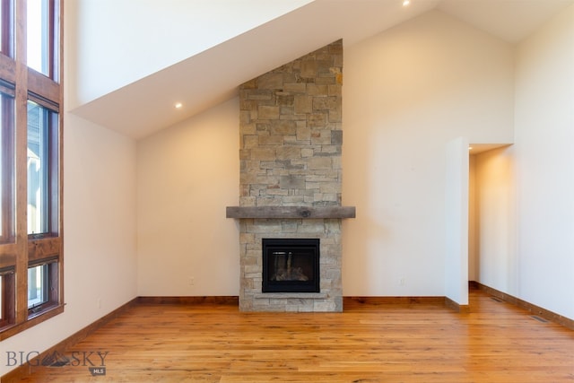 unfurnished living room with light hardwood / wood-style flooring, high vaulted ceiling, and a stone fireplace