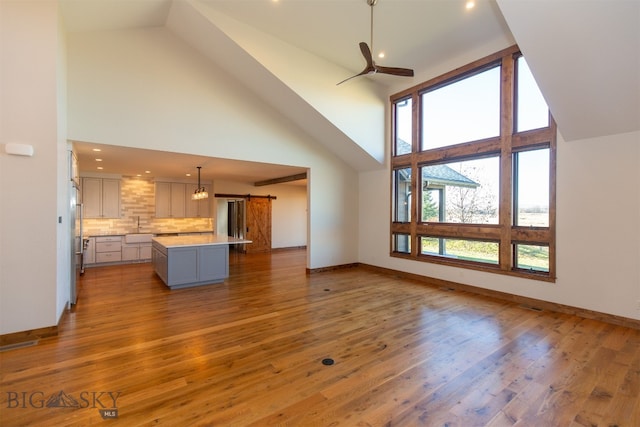 unfurnished living room with ceiling fan, sink, a barn door, high vaulted ceiling, and wood-type flooring