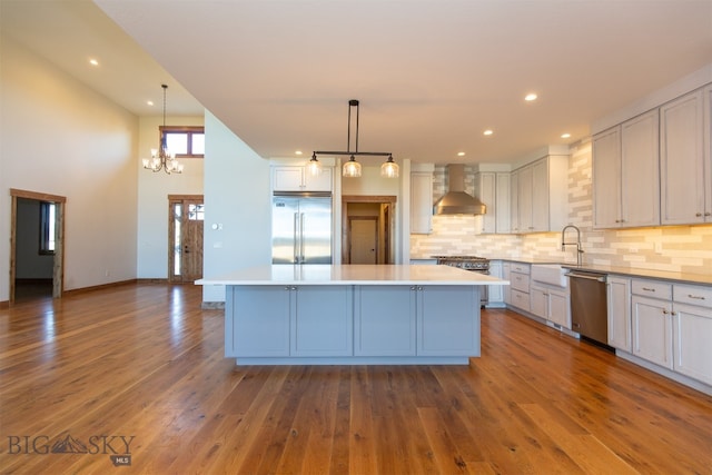 kitchen featuring a kitchen island, wall chimney range hood, stainless steel appliances, and dark wood-type flooring