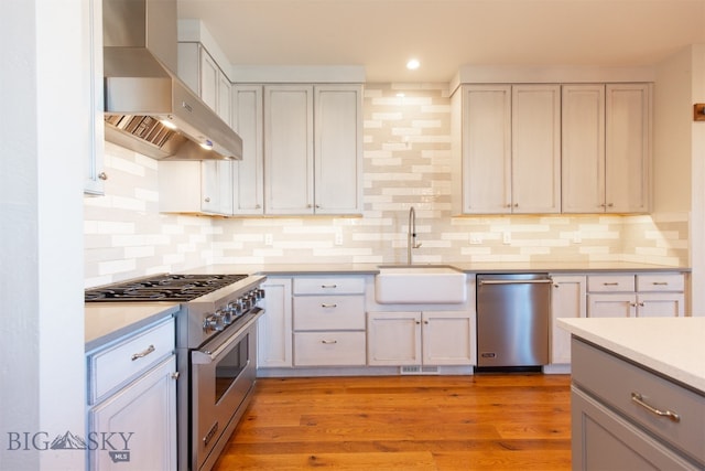 kitchen with decorative backsplash, stainless steel range, sink, wall chimney range hood, and light hardwood / wood-style flooring