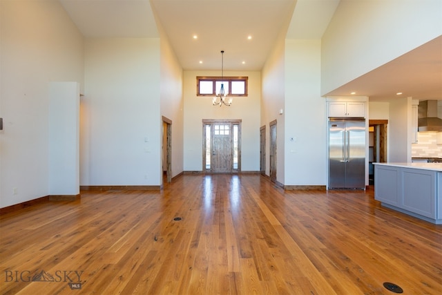 entryway with light hardwood / wood-style floors, a towering ceiling, and a chandelier