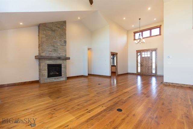 unfurnished living room featuring a fireplace, high vaulted ceiling, light hardwood / wood-style flooring, and a notable chandelier