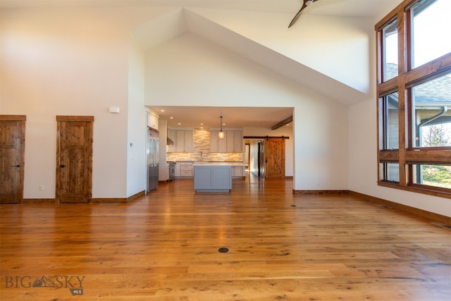 unfurnished living room featuring a barn door, light wood-type flooring, and high vaulted ceiling