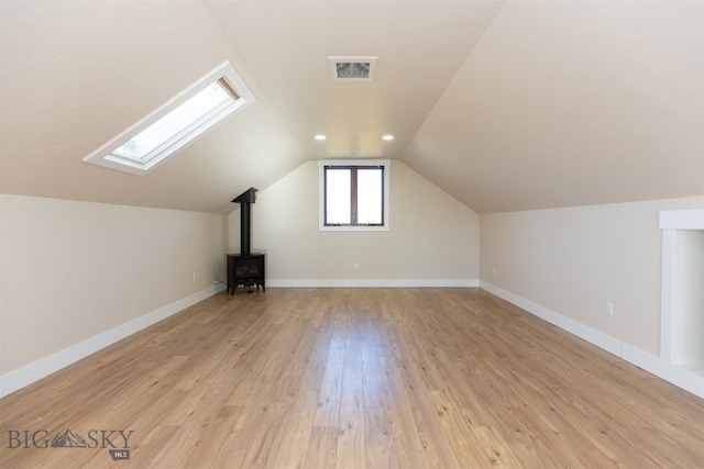 bonus room featuring light wood-type flooring, a wood stove, and lofted ceiling with skylight