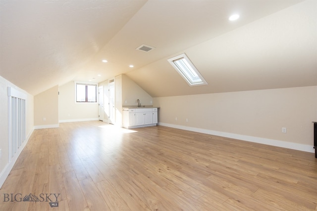 additional living space with sink, light hardwood / wood-style floors, and vaulted ceiling with skylight