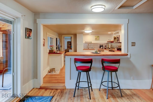 kitchen featuring decorative backsplash, light wood-type flooring, appliances with stainless steel finishes, kitchen peninsula, and a breakfast bar area