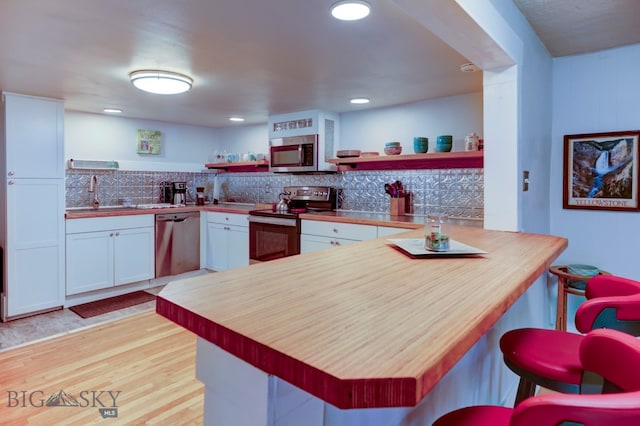 kitchen with kitchen peninsula, decorative backsplash, light wood-type flooring, stainless steel appliances, and white cabinetry