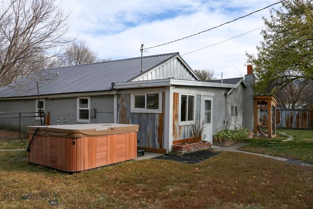 back of property with a hot tub and a lawn