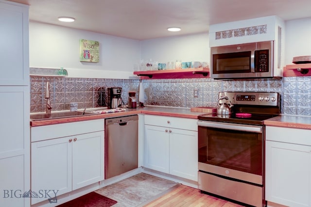 kitchen with white cabinets, stainless steel appliances, tasteful backsplash, and light hardwood / wood-style floors