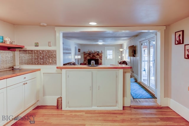 kitchen with tasteful backsplash, light hardwood / wood-style flooring, kitchen peninsula, a fireplace, and white cabinets