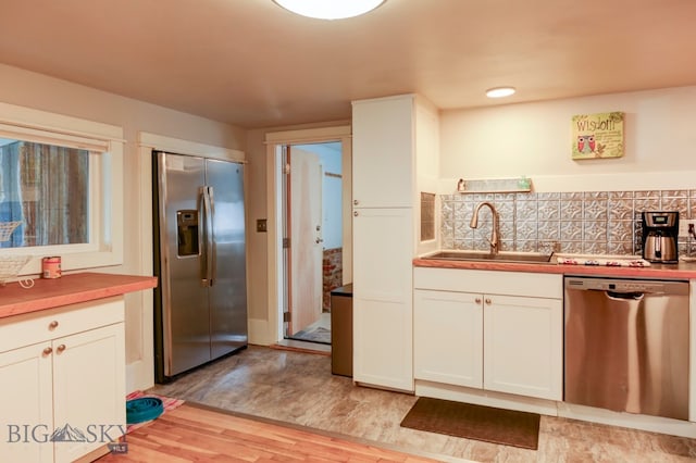 kitchen featuring appliances with stainless steel finishes, backsplash, sink, white cabinets, and light hardwood / wood-style floors