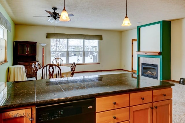 kitchen featuring ceiling fan, dishwasher, hanging light fixtures, carpet floors, and a tiled fireplace