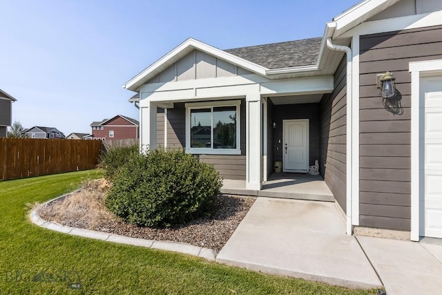 view of exterior entry with roof with shingles, a yard, a garage, and fence