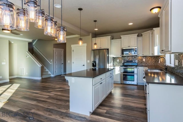 kitchen with dark wood-style flooring, dark countertops, white cabinets, stainless steel appliances, and a sink
