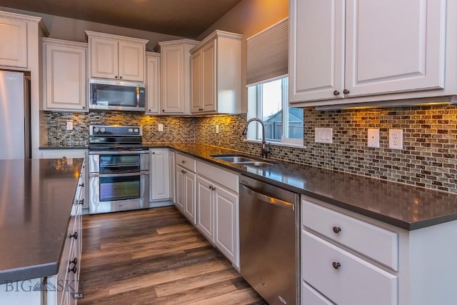 kitchen featuring stainless steel appliances, a sink, backsplash, and dark countertops