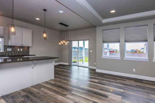 kitchen with a kitchen breakfast bar, dark wood-style flooring, dark countertops, baseboards, and backsplash